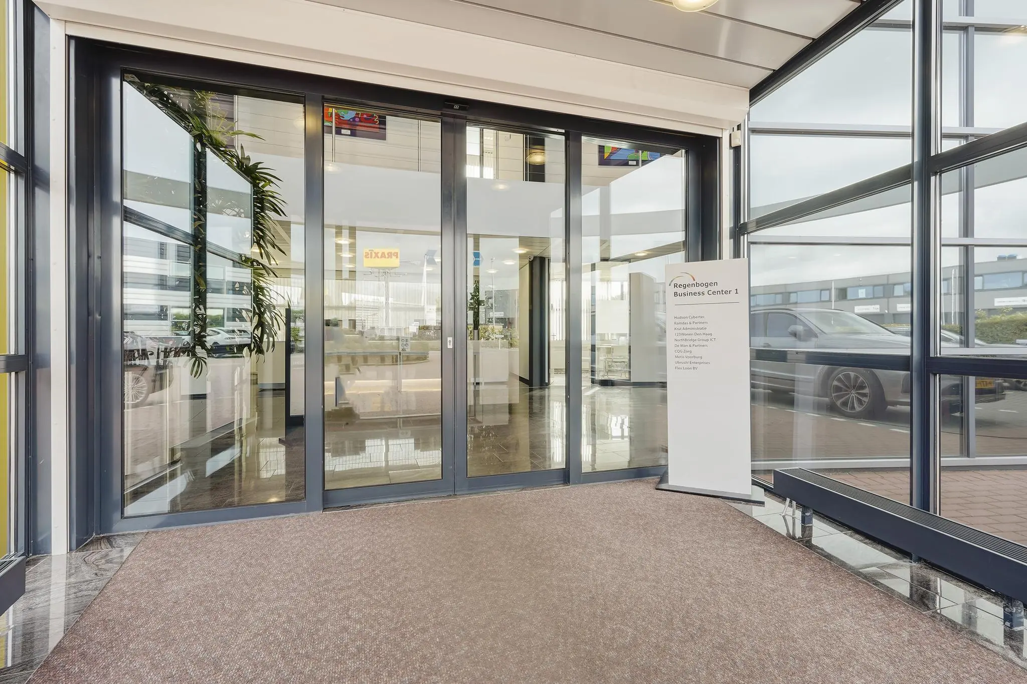 Ingang van Regenbogen Business Center 1 aan de Laan van 's-Gravenmade met glazen schuifdeuren en een informatief welkomstbord.